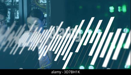Female technician wearing coat monitoring network on laptop in data center, with white graphic bars Stock Photo