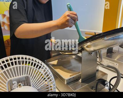 Balikpapan, Indonesia - Nov 16, 2025 A person in a black t-shirt is using a light blue silicone brush to apply batter or oil to the hemispherical mold Stock Photo