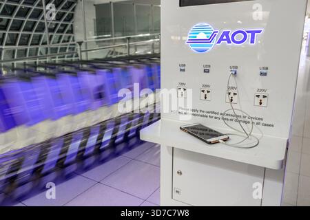 BANGKOK, THAILAND, JAN 16 2018, Charging phone on a charging station the AOT in airport terminal hall with moving row of luggage carts on a background Stock Photo