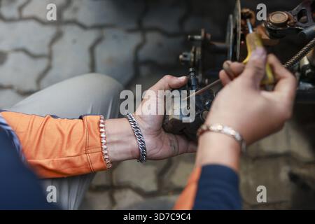 Focused technician hands repairing small engine component with screwdriver. mechanic works diligently outdoors on paved surface, showing manual labor Stock Photo