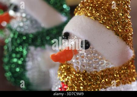 Cheerful gold sparkly snowman Christmas decoration for festive holiday. close up winter figure with an orange nose and happy expression on glitter bac Stock Photo