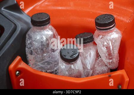 Four clear plastic bottles of cold water with black caps stored in an orange container. refreshing supply of cool hydration, healthy beverage ready fo Stock Photo