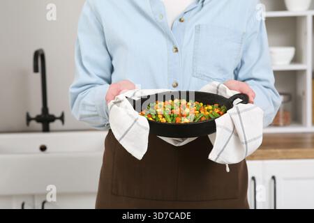 Young woman holding frying pan with roasted vegetables in kitchen Stock Photo