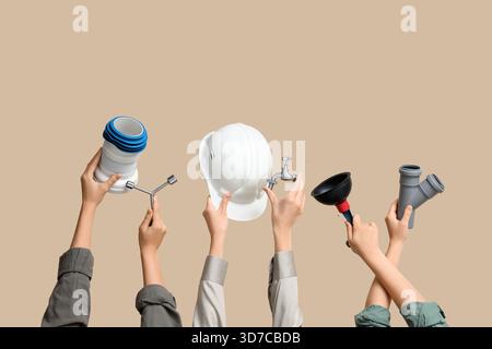 Hands with hardhat and plumber supplies on beige background Stock Photo