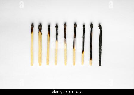 Conceptual image of burnout represented by a row of progressively burned wooden matches on a white background. Stock Photo