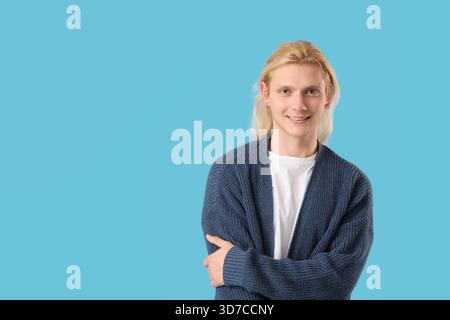 Young blonde man in cardigan on blue background Stock Photo