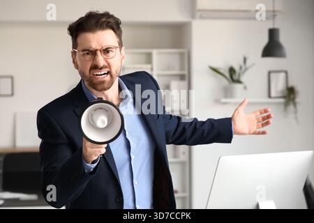 Angry businessman shouting into megaphone in office Stock Photo