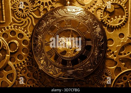 Gold antique pocket fob watch with gears and cogs in the background. Vintage industrial steampunk fashion accessories. Stock Photo