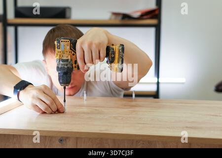 Close-up of male hand holding power drill driving screw into wooden surface during furniture assembly Stock Photo