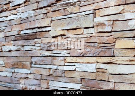 Close-up of a rustic stone wall made from stacked natural slabs in warm beige and brown tones, showcasing organic texture and earthy patterns. Stock Photo