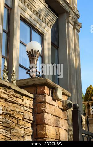 Close-up of elegant wrought iron street lamp with frosted glass globe mounted on stone pillar, showcasing classical architectural details in daylight Stock Photo
