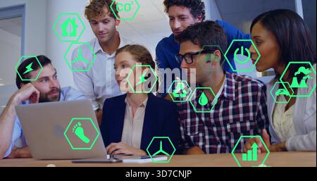 Collaborating six staff with navy blazer leaning over laptop at office table, showing green icons Stock Photo
