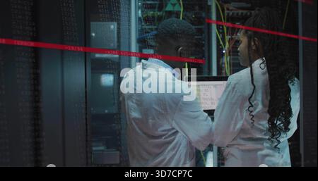 Two techs in white lab coats fixing servers in server aisle with yellow cables and laptop Stock Photo