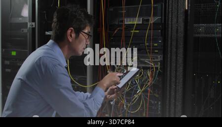Repairing Korean tech in blue shirt leaning into server rack, using tablet tracing Ethernet cables Stock Photo