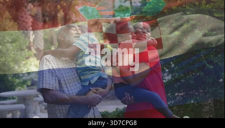 Smiling checked-shirt grandpa holding boy, red-dress woman holding girl in park, flag overlay Stock Photo