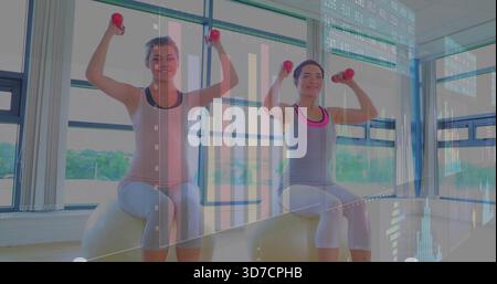 Lifting two women on exercise balls in tank tops pressing red dumbbells in studio, chart overlays Stock Photo