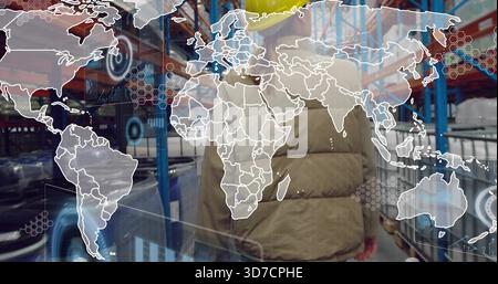 Walking worker in yellow helmet and puffer jacket, storage aisle with blue racks, digital overlay Stock Photo