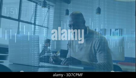 Working man wearing sweater typing on laptop at modern office desk, with notebook and data overlay Stock Photo