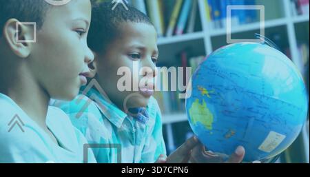 Examining two boys in light and blue plaid shirts, turning globe in classroom with shelf overlays Stock Photo