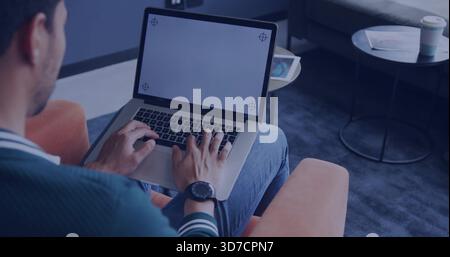 Typing man wearing green sweater on orange armchair in lounge, with laptop corner marks, copy space Stock Photo