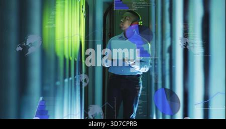 Technician in blue shirt inspecting racks in data center aisle, holding laptop with projected data Stock Photo