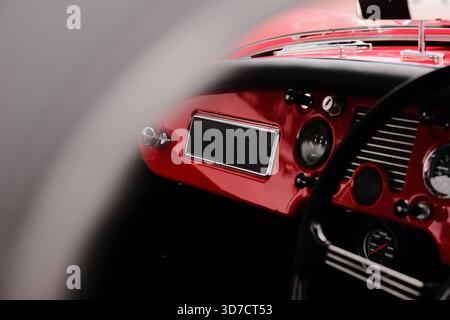 Close-up view of a classic car’s red dashboard, featuring retro gauges, chrome details, and a black steering wheel. Stock Photo