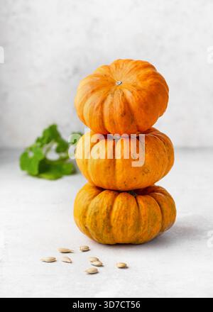 Stack of three small orange "Jack Be Little" pumpkins (Cucurbita pepo) on a bright surface, with a few scattered pumpkin seeds in front. Stock Photo