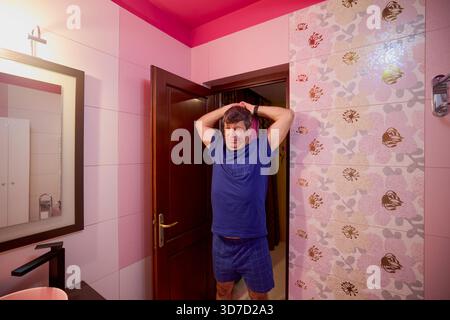 middle-aged man in the bathroom in the morning brushing his teeth, shaving and styling his hair Stock Photo