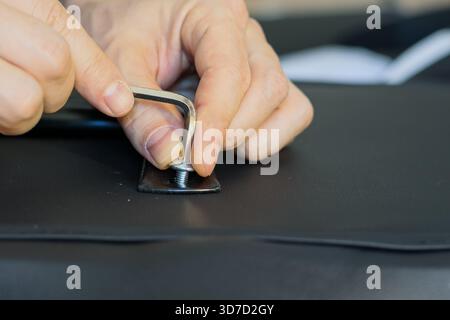 Detailed view of hands employing a wrench to fasten a screw on dark leather chair upholstery in repair process Stock Photo