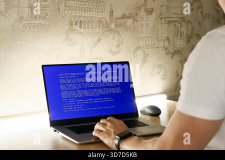 Individual working at desk with computer displaying system failure message on blue background Stock Photo