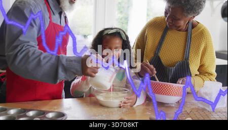 Mixing child holding glass bowl at home, senior pouring from measuring cup and stirring with aprons Stock Photo