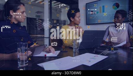 Discussing three women in business attire reviewing charts at conference table with laptop, tablet Stock Photo