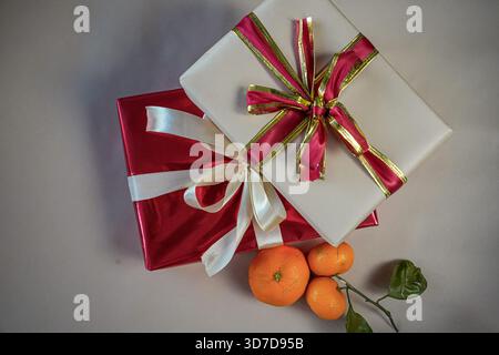 Top view of beige and red gift boxes with ribbons placed together on a neutral beige background. Three fresh tangerines with a small green twig lie ne Stock Photo