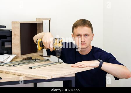Carpenter using power drill to fasten drawer slide on wood board. Carpenter in dark shirt using power drill to fasten metal drawer slide onto wooden b Stock Photo