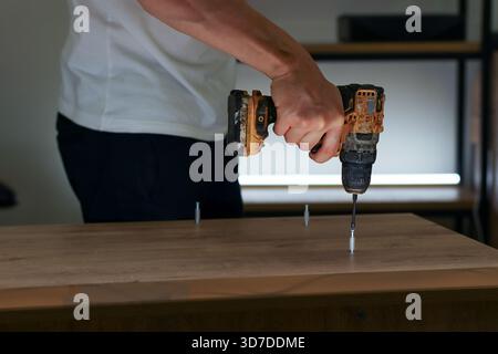 Worker assembling furniture by drilling screws into wood, viewed from side in indoor setting Stock Photo