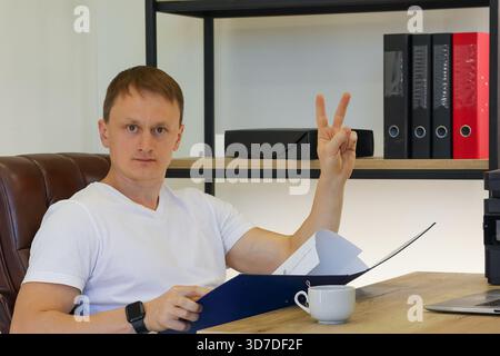 Office employee raising index finger in attention gesture with paperwork and beverage on table Stock Photo