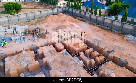 Aerial view of construction workers busy on a construction site with foundation trenches, surrounded by walls and buildings, Katsina, Katsina, Nigeria Stock Photo
