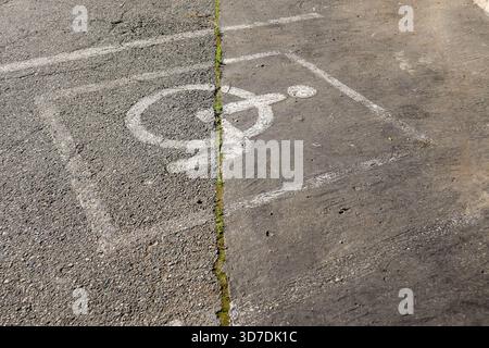 Detailed view of a deteriorating disabled parking spot on uneven asphalt, featuring a partially erased blue wheelchair icon surrounded by sprouting we Stock Photo