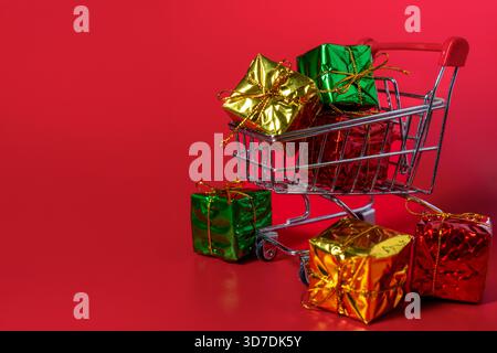 A shopping cart filled with wrapped gift boxes on a red background. Christmas shopping, holiday sales, and festive season purchases concept. Stock Photo