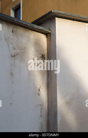 Textured beige wall with visible cracks, peeling layers, and weathered patina on an urban building exterior in daylight. Stock Photo