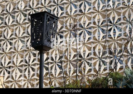 Decorative black lantern post silhouetted against intricate white geometric building facade and sparse autumn branches. Stock Photo