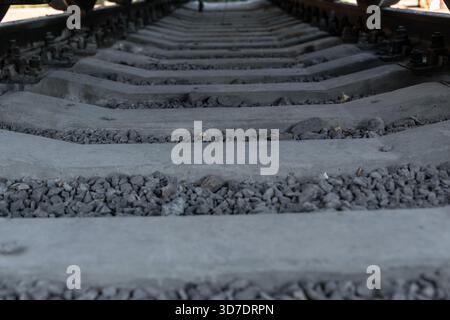 Low angle view of empty railway tracks with grey gravel and concrete sleepers, ideal for transportation, industry, or travel concepts. Stock Photo