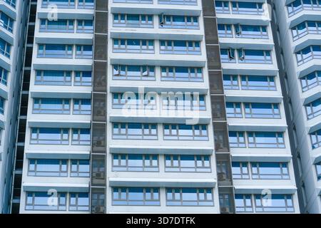 A contemporary residential building features numerous large windows. The structure stands tall against a clear blue sky. Sunlight highlights the sleek Stock Photo