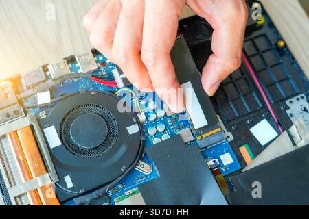 Laptop repair engineer PC computer and motherboard install random access memory ram ssd in computer lab top. The master installs the disk in his hands Stock Photo