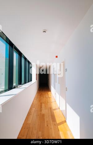 Modern minimalist hallway with wooden flooring and white walls, illuminated by natural sunlight streaming through large windows. The clean architectur Stock Photo