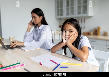 Woman Works on Laptop While Daughter Looks Bored at Home During Day Stock Photo