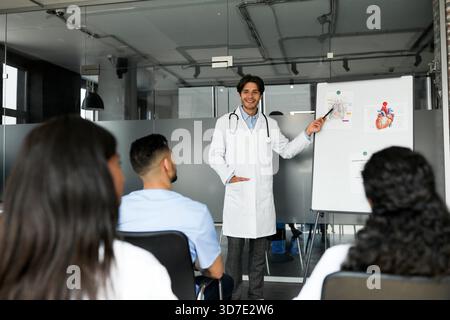 Cheerful man doctor standing next to presentation board, having speech Stock Photo