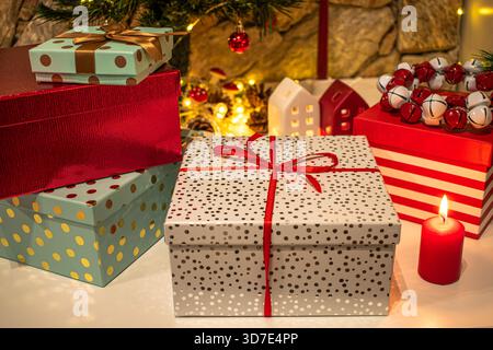 Christmas gifts, bright boxes with ribbons. A candle and festive decorations in the background. Stock Photo