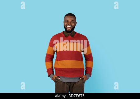 Positive black man standing with hands in pockets and smiling at camera Stock Photo