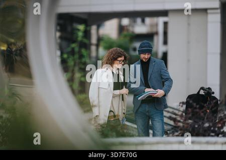 Two professionals review documents outdoors in a city setting, collaborating on a business project today. Stock Photo